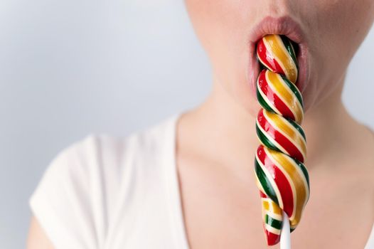 Close-up portrait of a woman sucking a long lollipop against a white background. Blowjob simulation.