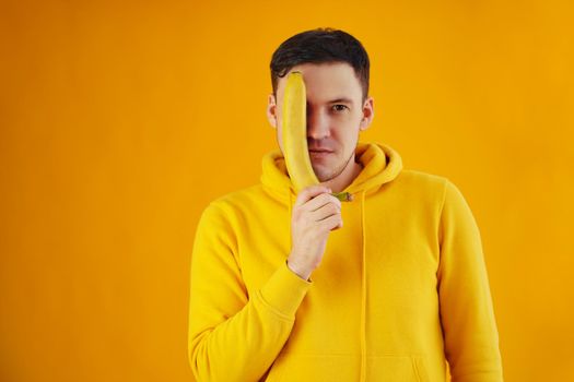 Portrait of young man with banana on yellow background. Funny guy in yellow hoodie posing wth fruit