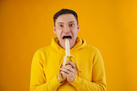 Portrait of young man with banana on yellow background. Funny guy in yellow hoodie posing wth fruit