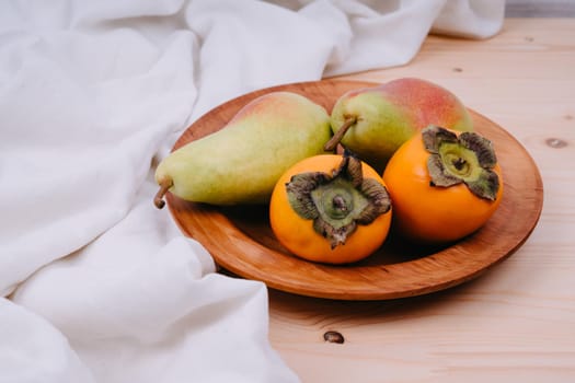 Wooden plate with fruit. Persimmons and pears. Eco-friendly tableware. Plate made of natural material.