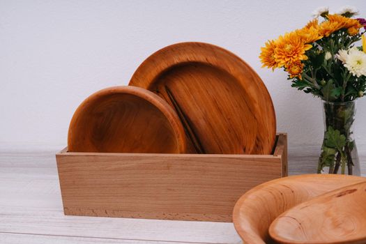 Wooden dishes in a box and a bouquet of autumn flowers. Plates made of natural material. Chrysanthemums.