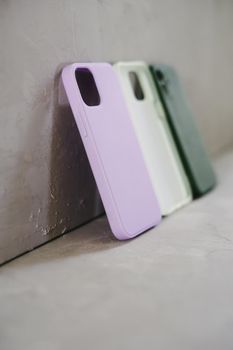 Three silicone cases to protect the smartphone from falls and shocks. Green, white and lilac covers on a gray background.