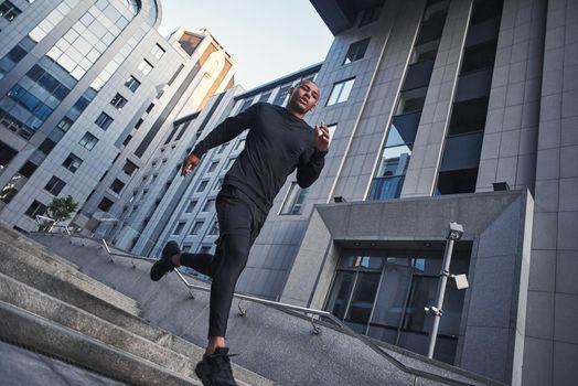 Cardio training. Full length of young african man in sportswear running in the morning against modern buildings of the city. Workout. Sport concept. Health concept