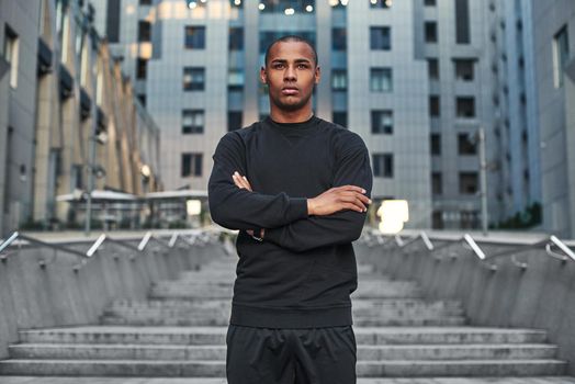 Sport is the way of life. Athletic african man with a muscular body standing on stairs with crossed arms and ready to start his morning workout. Sport concept. Health concept. Lifestyle. Urban workout