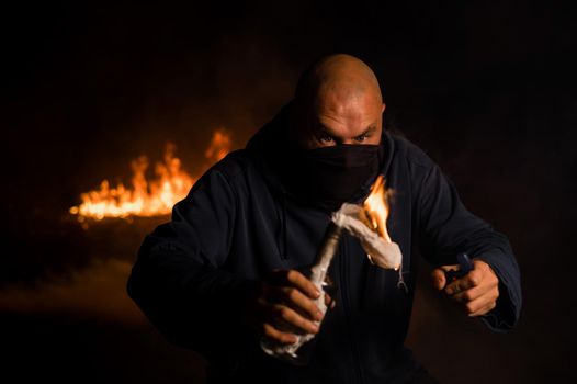 A masked man is holding a burning bottle. Molotov cocktail