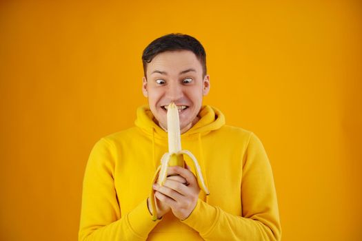 Portrait of young man with banana on yellow background. Funny guy in yellow hoodie posing wth fruit