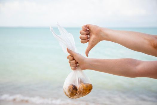 hands hold a plastic bag with fruits and show a thumb down against the background of the sea. no face. the concept of pollution of nature and a conscious attitude to the ecology of the planet.