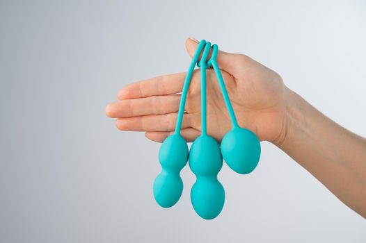 A faceless woman demonstrates a set of mint-colored vaginal balls. Girl holding a kegel trainer for training pelvic floor muscles on a white background