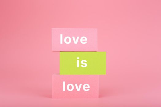 Love is love written on stack of yellow and pink rectangles on pink background. Concept of Lgbtq pride social post, tolerance, respect and equal rights