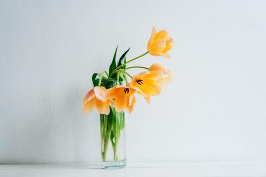 A bouquet of orange tulips in a vase on a white wooden table. Happy Mother's Day. March 8. Holiday card.