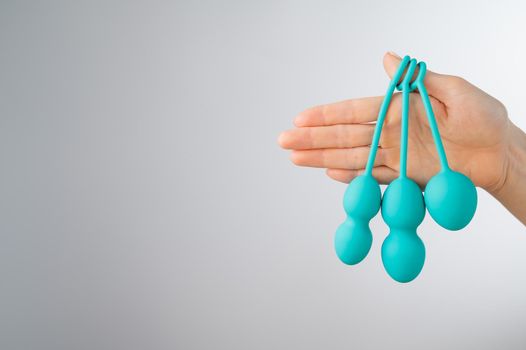 A faceless woman demonstrates a set of mint-colored vaginal balls. Girl holding a kegel trainer for training pelvic floor muscles on a white background
