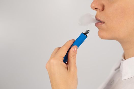 Caucasian woman smokes disposable vape on white background. Alternative device for smoking