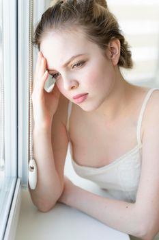 sad young woman holding her head by the window. migraine and headache