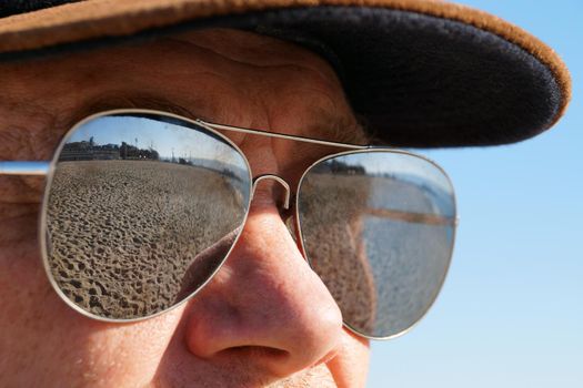 a man in sunglasses reflecting the sandy shore, portrait