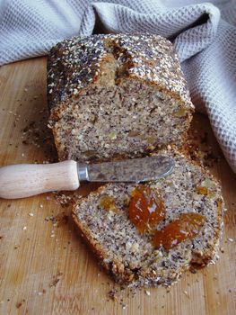 Whole grain organic bread with homemade poppy seeds. Appetizing slice of bread with a portion of jam, small serving knife with wooden handle, wooden surface.