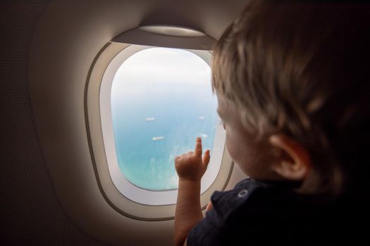 resumption of flights, opening of borders concept. a small child looks at the ocean from the window of a flying plane. first flight. vacation happiness. soft focus