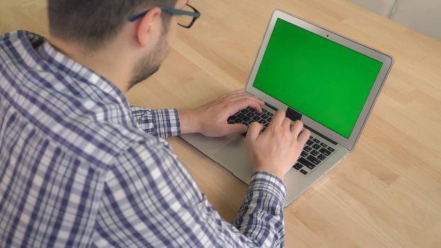 Casual stylish guy typing on keyboard laptop with green screen