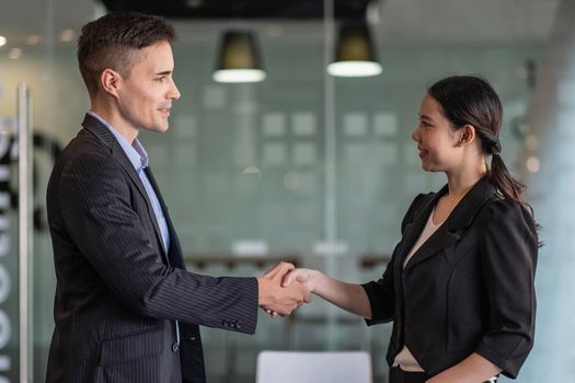 Happy positive business partners finishing meeting. Business man and woman standing in office, shaking hands, smiling, talking. Handshake concept.