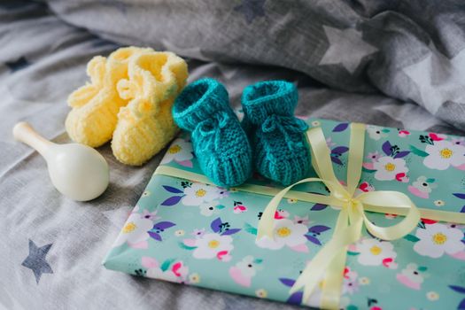 Knitted yellow and blue booties for baby. Maracas and a gift tied with a ribbon.