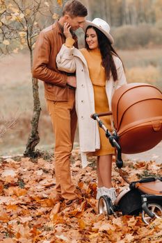 Father and mother on a walk with a stroller in the autumn Park. The family walks through the nature Park in the Golden autumn