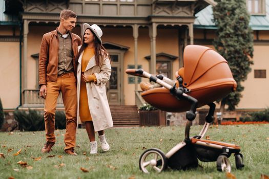 Father and mother on a walk with a child in a stroller in the autumn Park on the background of the estate. A family walks through the Golden autumn nature Park.