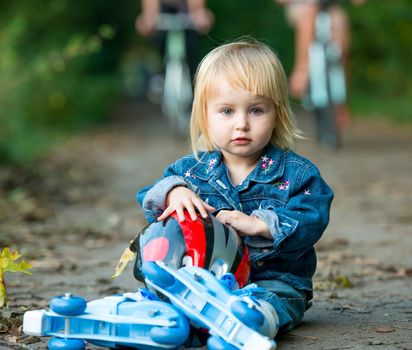 Cute little girl on roller skates sitting on road in the park