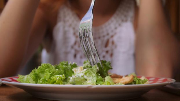 Unrecognizable woman eating salad. Close up woman hand with a fork sticks vegetables.