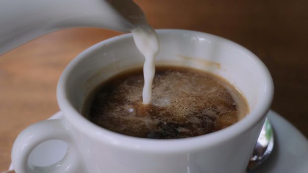 Close up details milk pouring into cup with coffee.