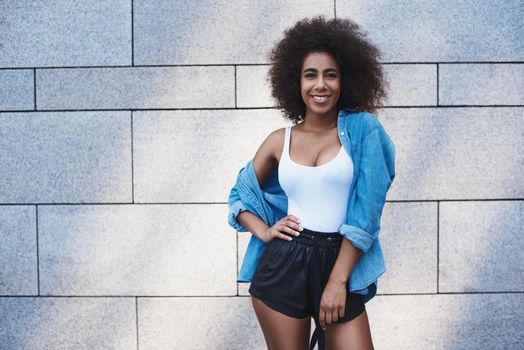 Young woman free style on the street standing isolated on concrete wall posing hand on hip looking camera smiling happy