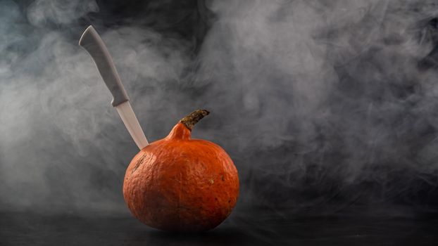 A knife in a pumpkin in the smoke. Happy Halloween