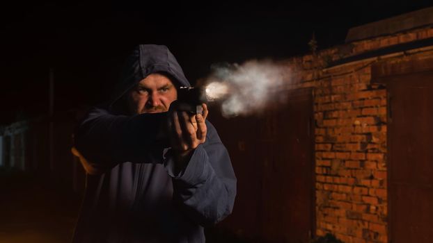 Caucasian man in a hood shoots a pistol