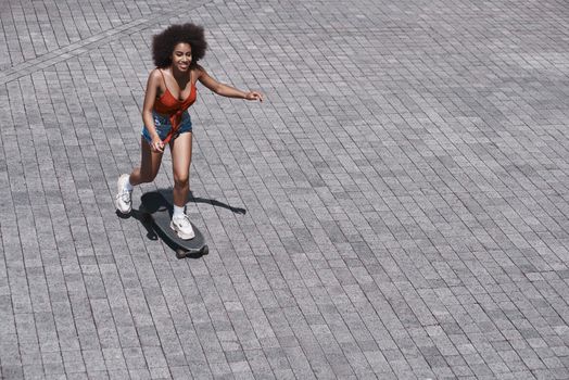 Young woman free style on the street riding skateboard on the paved road smiling excited top view