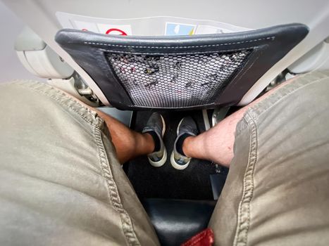 The legs of a man sitting in an airplane. Economy class and narrow spaces between the seats. Sports and summer clothing.