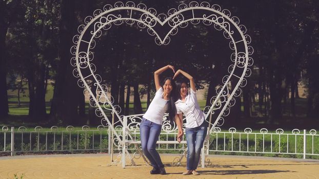 Two happy friends make sign heart in park.