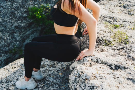 A girl in a black suit and white sneakers is engaged in sports in the mountains. Outdoor sports. The girl performs a sports exercise.