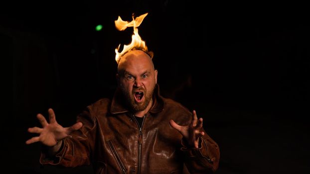 Bald man in a leather jacket with a burning head on a dark background