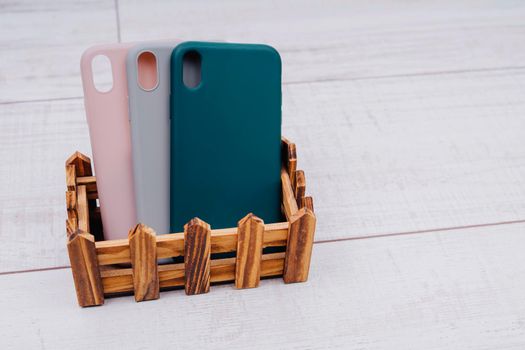 Three silicone cases for a smartphone stand in a wooden stand. Grey, green and pink smartphone cases. Protect your phone.