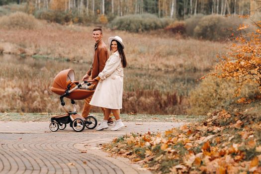 Father and mother on a walk with a stroller in the autumn Park. The family walks through the nature Park in the Golden autumn