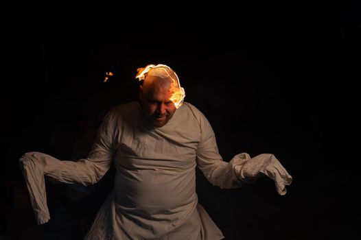 Bald man in a straitjacket with a burning head on a dark background