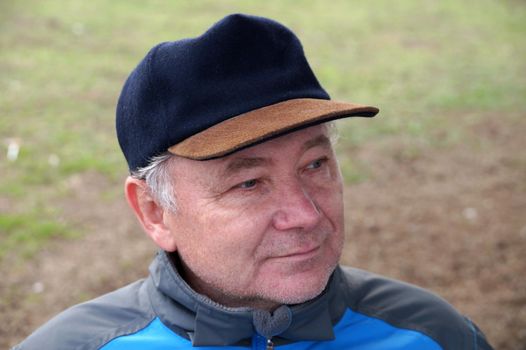 portrait of a smiling middle aged man in a cap on a natural background
