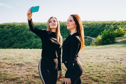 Girls in black tracksuits take selfies on a smartphone. Girls actively relax in nature.