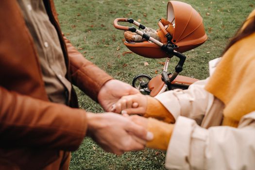 Father and mother hold hands near a stroller with a child on a walk in the autumn Park. A family walks through the Golden autumn nature Park