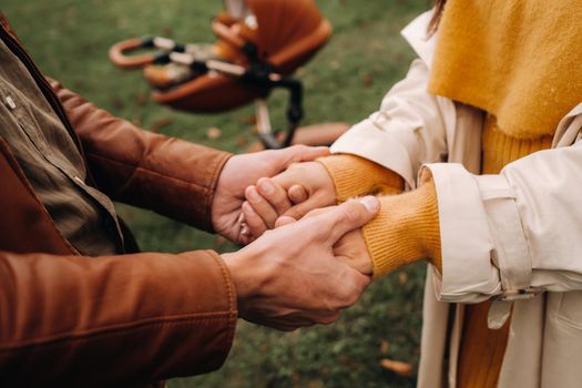 Father and mother hold hands near a stroller with a child on a walk in the autumn Park. A family walks through the Golden autumn nature Park