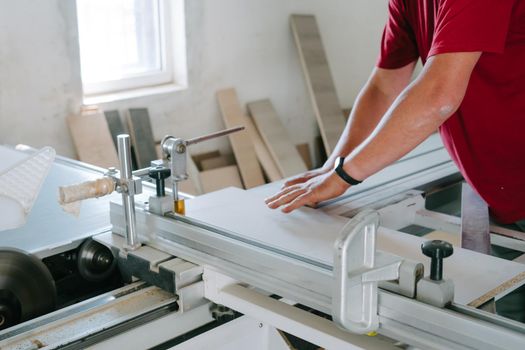 Work in the furniture shop. Furniture production. A man in a red T-shirt works behind a machine to produce modular furniture.