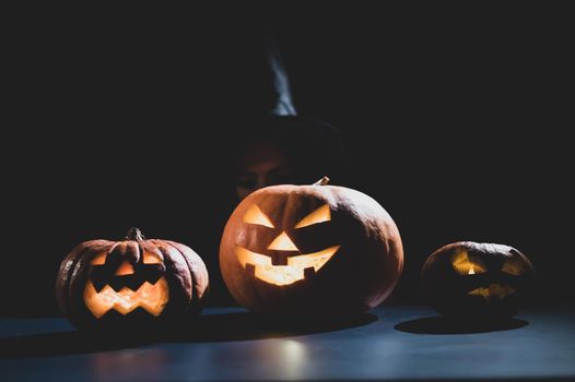 The evil witch casts a spell on pumpkins. Portrait of a woman in a carnival halloween costume in the dark.