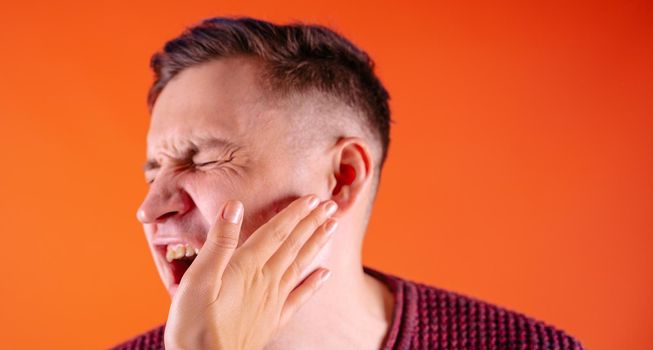 Crop person slapping scared man in face. Emotional male getting slapped in face while shouting with closed eyes in fear on orange background.