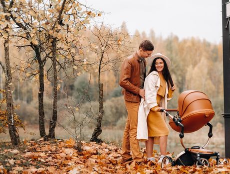 Father and mother on a walk with a stroller in the autumn Park. The family walks through the nature Park in the Golden autumn