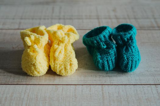Yellow and mint knitted booties on the wooden floor. Knitted socks for the baby.