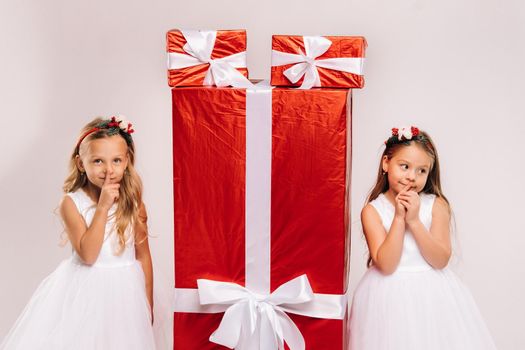 two little girls with Christmas gifts on a white background and a huge gift.