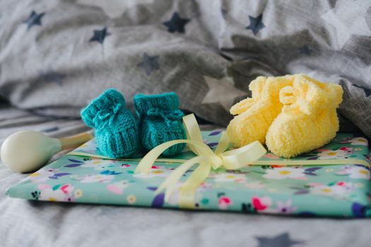Knitted yellow and blue booties for baby. Maracas and a gift tied with a ribbon.